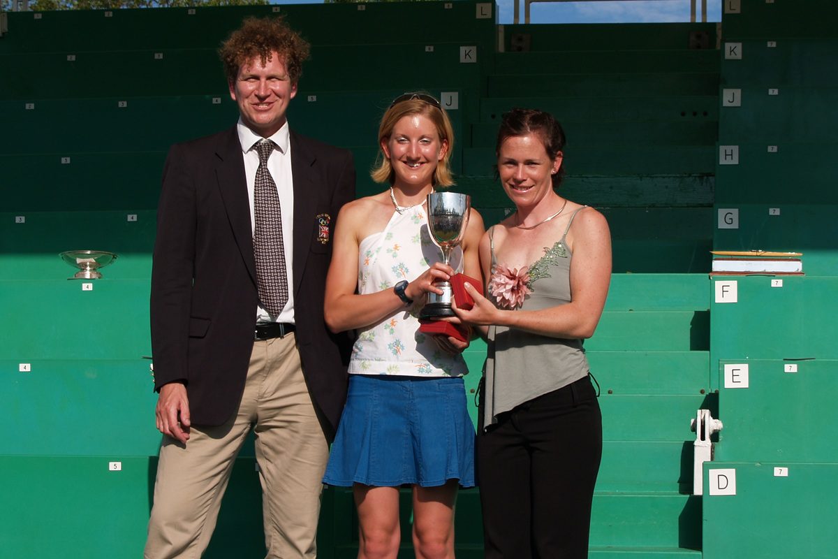 Man in navy blazer presenting 2 women with trophy