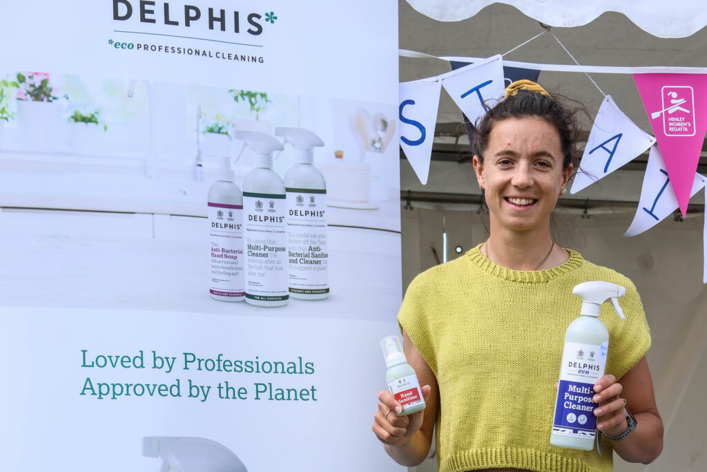 A woman in a yellow top holds two spray bottles in front of a backdrop advertising environmentally friendly cleaning products