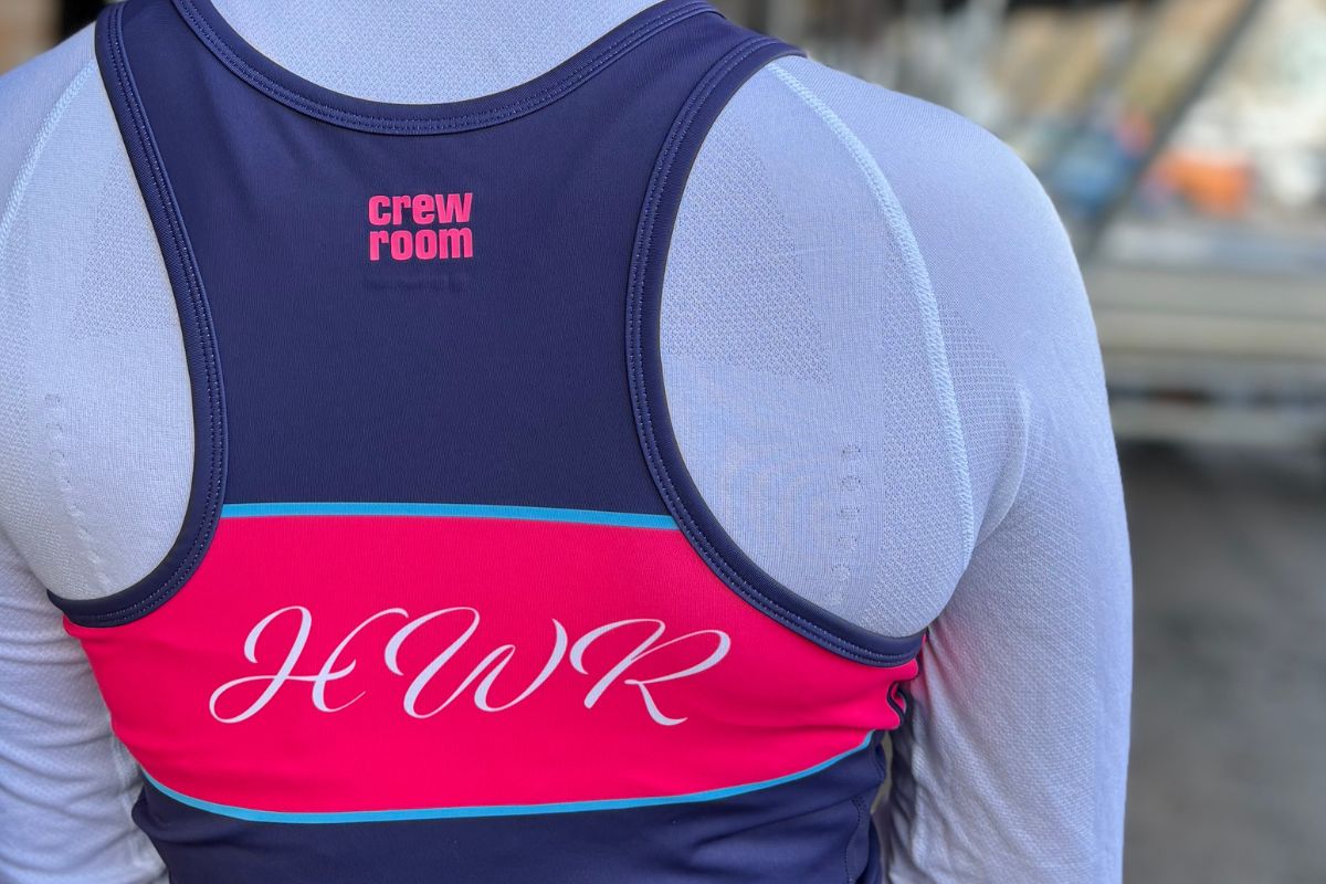 A rower is seen from behind wearing a navy and pink rowing suit, with 'HWR' in italic white writing on the pink band.