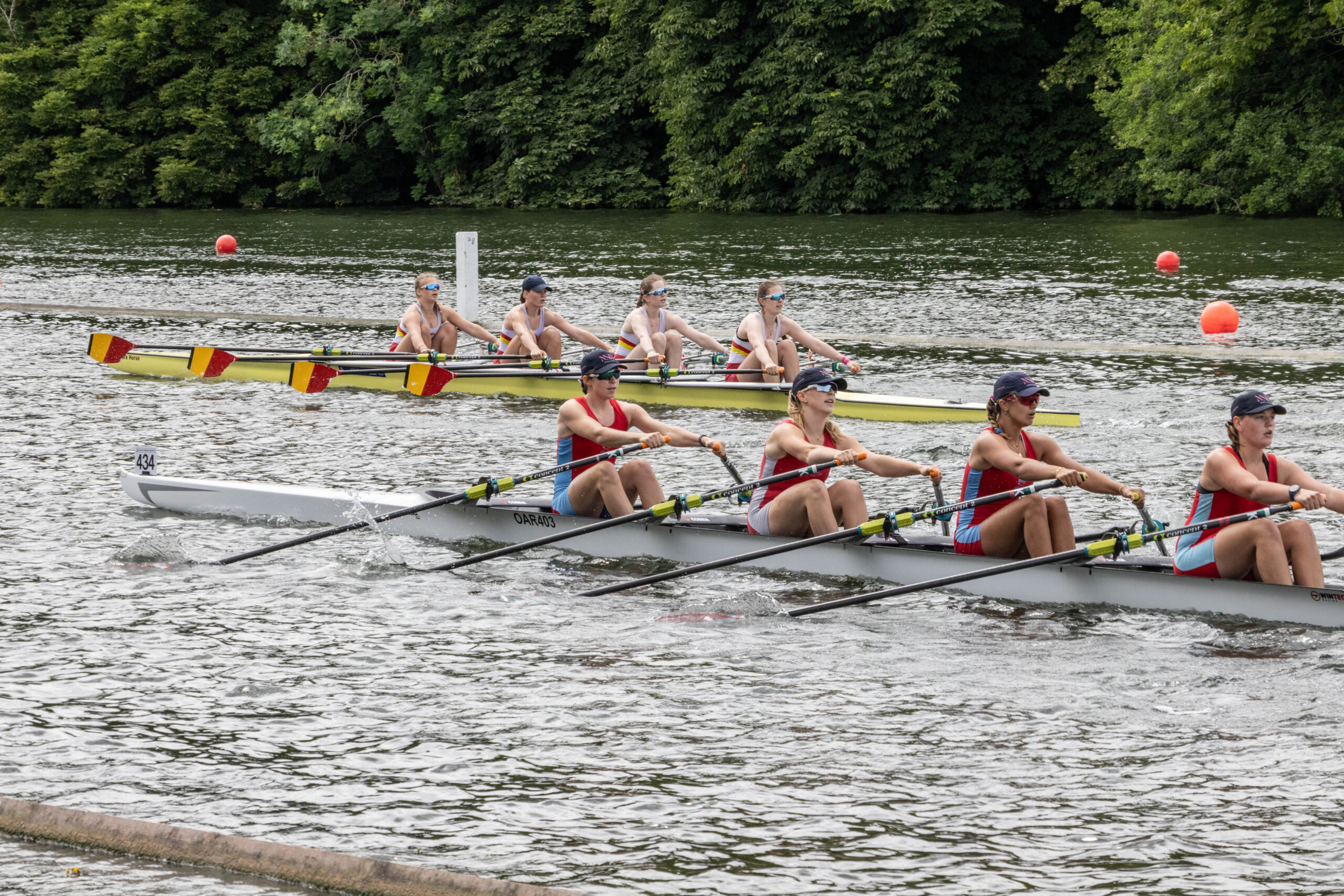 Two junior women's quadruple sculls race away from the camera.