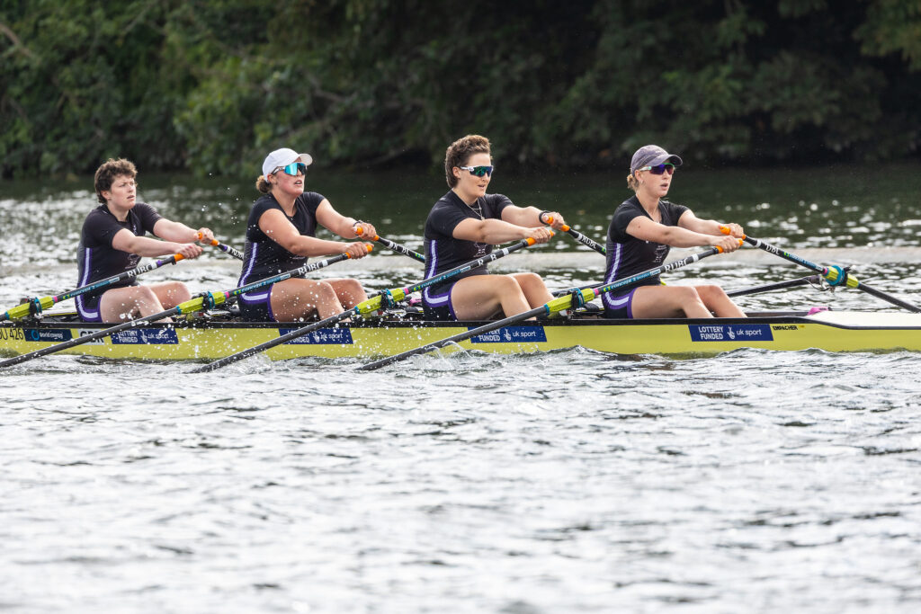 Four women in black and purple unisuits row a quadruple scull