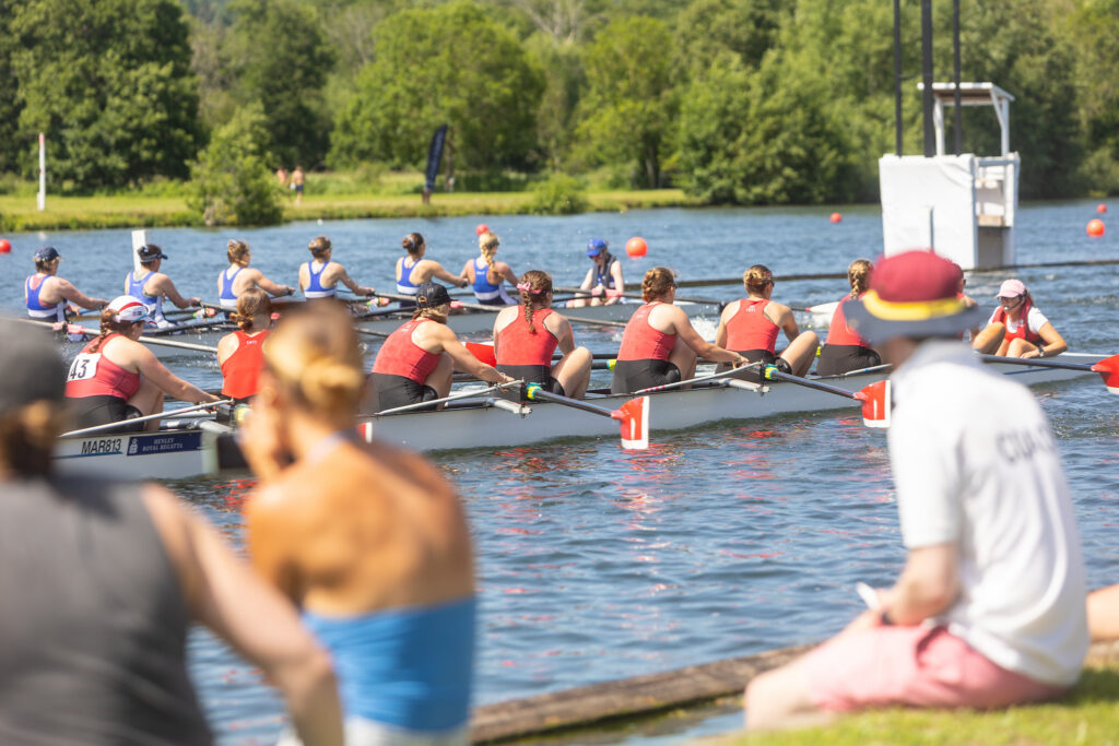 Spectators sit on the bank watching two women's eights race